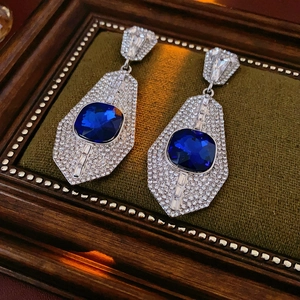 Detail of square blue gemstone earrings with rhinestones on green velvet background