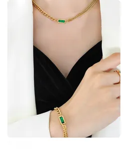Detail of model wearing gold chunky double-layer necklace with emerald green gemstone set
