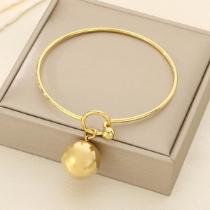 Close-up of golden metallic bangle featuring a large hollow sphere pendant and round knot