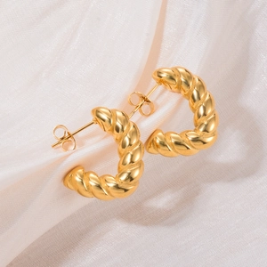 Detailed view of gold twisted C-shape earrings on soft pink satin fabric background