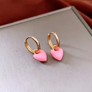 French vintage gold hoop earrings with pink enamel heart charms on a textured background