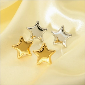 Minimalist gold and silver 3D star-shaped earrings on elegant gold silk fabric