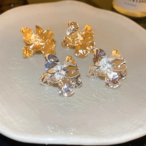 Macro detail of gold and silver textured flower earrings on a white ceramic plate