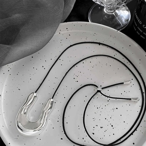 Irregular silver U-shaped pendant on a black adjustable cord, presented on a ceramic tray