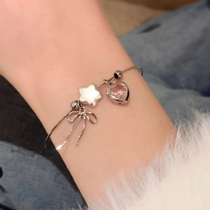Close-up of silver bangle with zircon heart, star, and bow charms on wrist