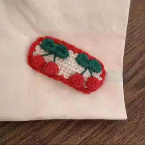 Detailansicht der handgestrickten Haarklammer mit gesticktem roten Kirschmuster