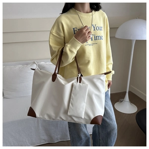 Beige nylon tote bag with brown leather handles worn by model in a cozy home setting