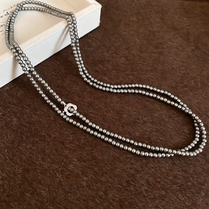 Detailed macro view of layered gray beaded necklace with a silver floral clasp ornament