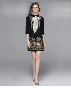 Detail of colorful floral embroidery on black long-sleeve dress with white silk bow