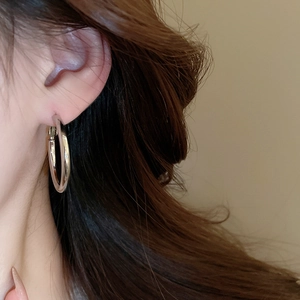 Close-up of minimalist large round gold hoop earrings worn by a model in soft lighting