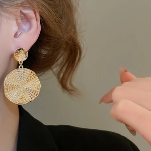 Detailed close-up of gold geometric drop earrings with spiral texture on a female model