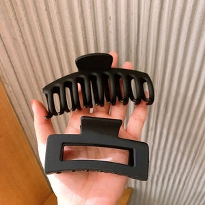 Close-up of two large matte black shark hair claws being held for size comparison
