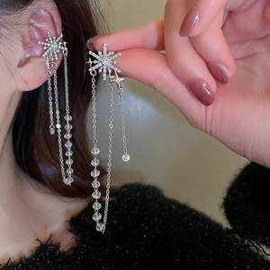 Gros plan sur des boucles d'oreilles à pompon argenté avec flocons et étoiles