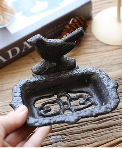 Close-up of vintage cast iron bird soap dish with drainage holes on a wooden table