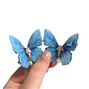 A pair of blue butterfly hair clips featuring pearls and rhinestones on metal duckbill clips