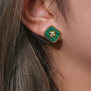 Close-up of vintage gold-plated star earrings with green striped resin on a model