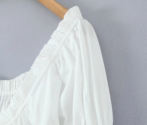 Détail des manches bouffantes et de l'encolure froncée sur une robe blanche