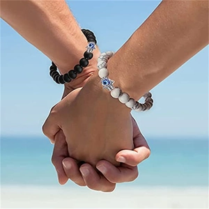 Couples natural stone bracelets with evil eye Hamsa charms on a beach background