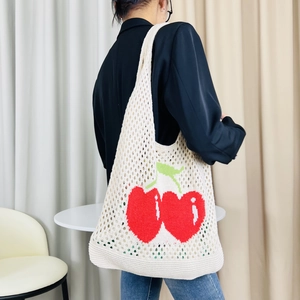 Close-up of cream knit tote bag with red cherry patterns worn on the shoulder