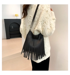 Detailed view of black tassel shoulder bag featuring lychee grain leather on white sweater