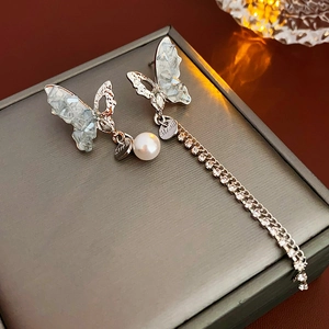 Macro view of asymmetrical silver butterfly earrings with pearls and crystal tassels