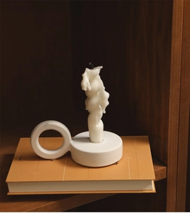 Detail of white ceramic ring holder with artistic melting candle on an orange book