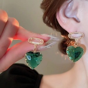 Close-up of heart-shaped green crystal earrings with gold plating on a model