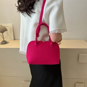 Rose red shell bag with crocodile pattern and adjustable strap worn by a model