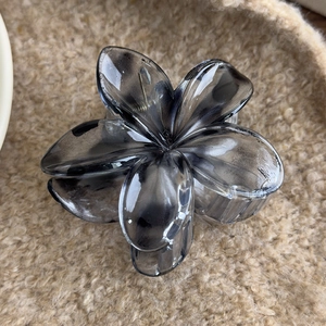 Detail of dark grey translucent flower hair claw clip on soft textured background