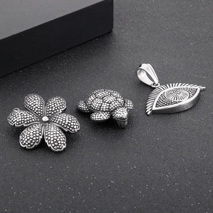 Detail view of retro turtle, flower, and evil eye stainless steel pendants with dotted texture
