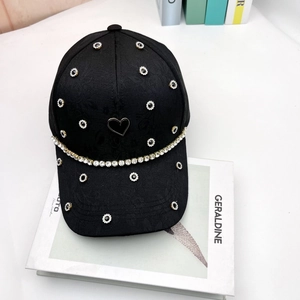 Detail of black baseball cap featuring floral texture, rhinestone chain, and a heart ornament