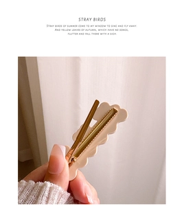 Detail view of cream wavy hair clip with golden metal fastener and text decoration