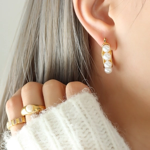 Elegant gold titanium earrings with pearls and matching rings on a female model