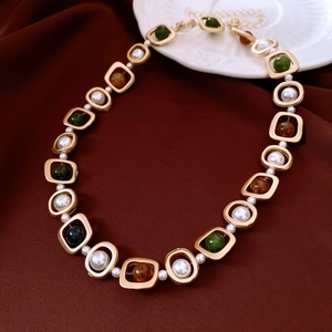 Détail d'un collier vintage doré avec perles émeraude et nacre sur tissu rouge