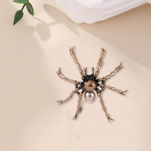 Broche araignée dorée vintage avec perle champagne et cristaux noirs sur fond neutre chic