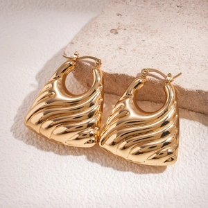 Macro detail of golden geometric earrings featuring textured wavy patterns and metallic luster