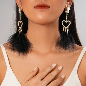 Close-up of heart-shaped rhinestone earrings with elegant black feather tassels on model