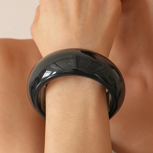 Polished black resin bangle bracelet with wide circular design on female wrist
