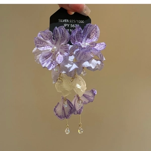 Dettaglio di orecchini lunghi a fiore con petali in tessuto viola e perle preziose
