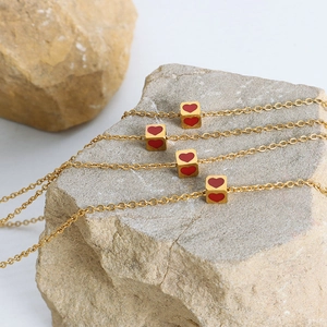 Minimalist gold cube pendant necklace with red hearts displayed on natural stone