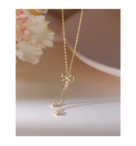 Macro detail of golden S925 bow necklace with zircon tassels on cream background