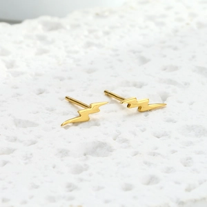 Macro shot of minimalist gold lightning bolt earrings on a white textured stand