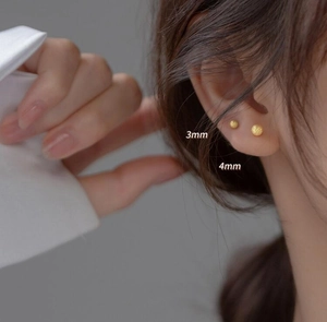 Close-up of 3mm and 4mm matte gold ball stud earrings on a model's ear