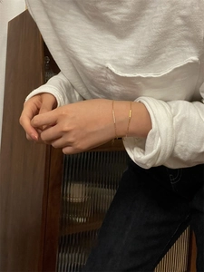 Detailed view of a minimalist gold thin chain bracelet with a cylindrical metal bar