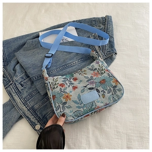 Close-up of floral jacquard shoulder bag with blue strap and brand label on denim