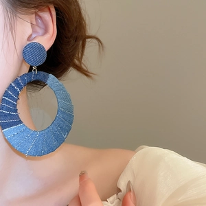 Close-up of model wearing denim oval earrings with white stitching details