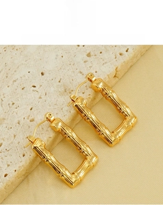 Détail macro de boucles d'oreilles dorées à texture bambou sur support en pierre épuré
