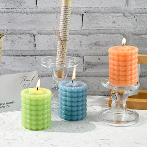 Dettaglio di tre candele cilindriche a bolle colorate con trama a cuore su supporti
