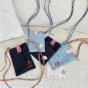 Detail of embroidered denim bags featuring cherry, rabbit and colorful beaded straps