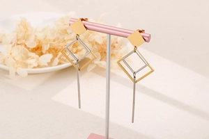Detail of minimalist geometric square earrings in gold and silver on a jewelry stand